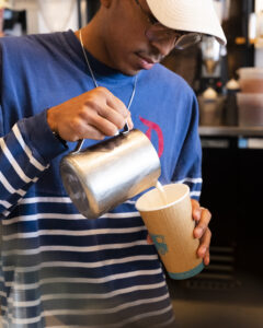 Barista pouring milk into a cup with espresso