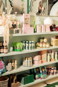 Shelf with Mandy's merch like salad dressing, cookbooks, and other non-Mandy's items like Boom Chicka Pop popcorn, Fly by Jing chili oil